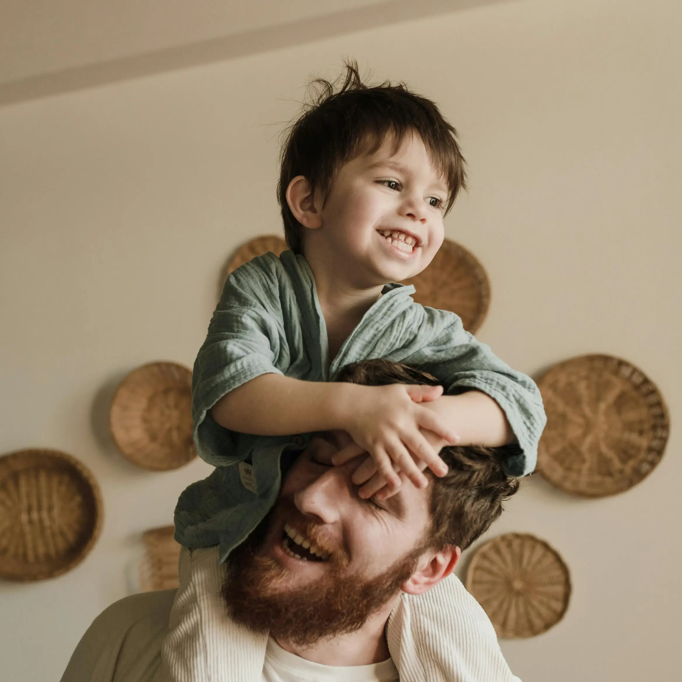 A smiling adult holding a young child on their shoulders inside a home